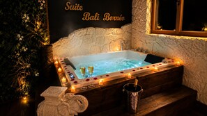 Un bain à remous agrémenté de pétales de rose et de bougies, une statue et une pancarte indiquant « Suite Bali Bornéo ».