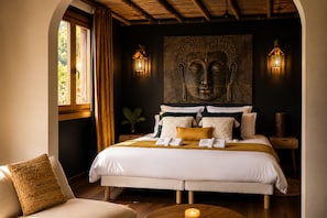 Ein Schlafzimmer mit einem großen Bett, zwei Wandleuchten, einer Buddha-Statue an der Wand und einem Fenster mit Vorhängen.