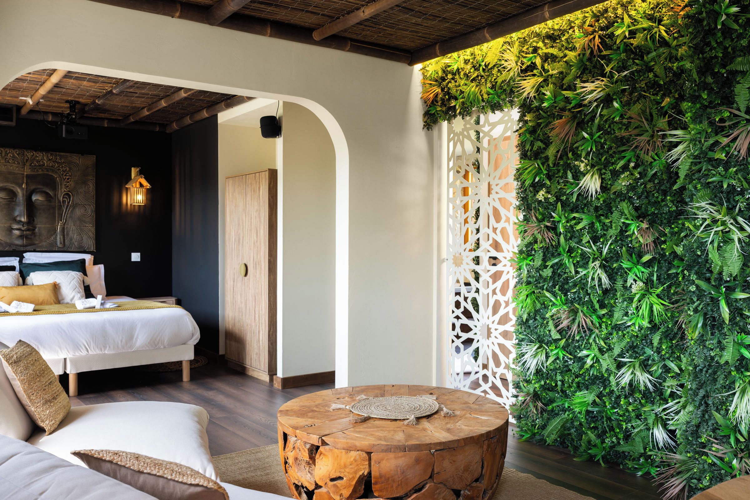 A modern bedroom with a bed, a wooden headboard, a round wooden table, and a green wall with plants.
