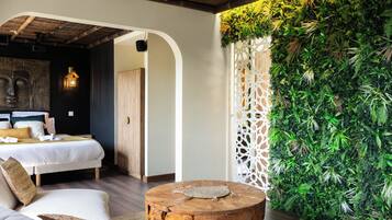 A modern bedroom with a bed, a wooden headboard, a round wooden table, and a green wall with plants.