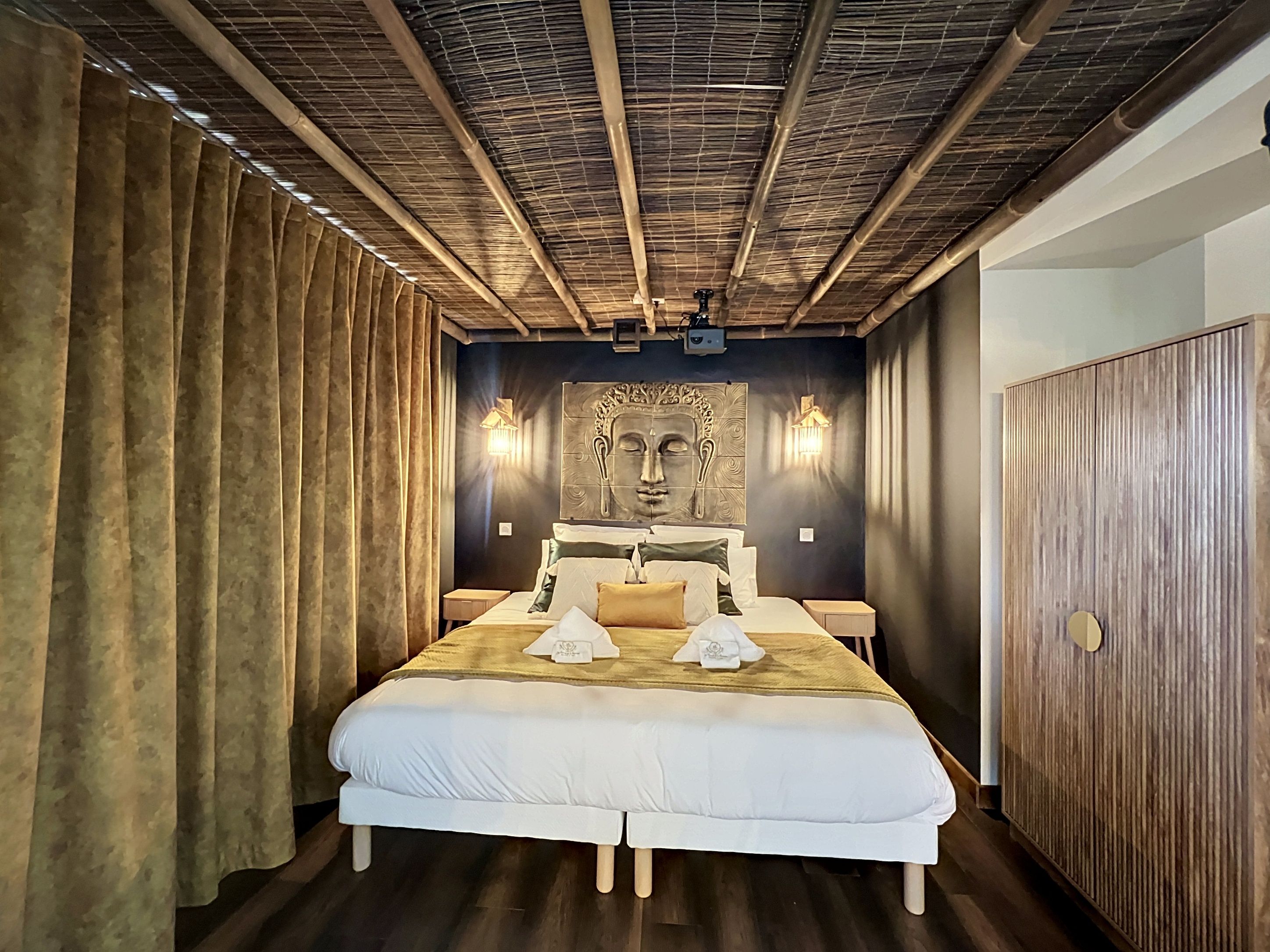 A hotel room with a large bed, two bedside tables, a wall-mounted light fixture, and a wooden door.