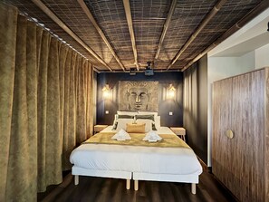 Une chambre d’hôtel avec un grand lit, deux tables de chevet, un luminaire fixé au mur et une porte en bois.