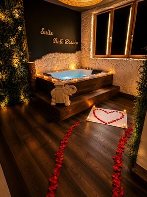 Une suite de spa avec un mur en pierre, une baignoire et une décoration en forme de cœur, réalisée avec des pétales de roses disposés sur le sol.