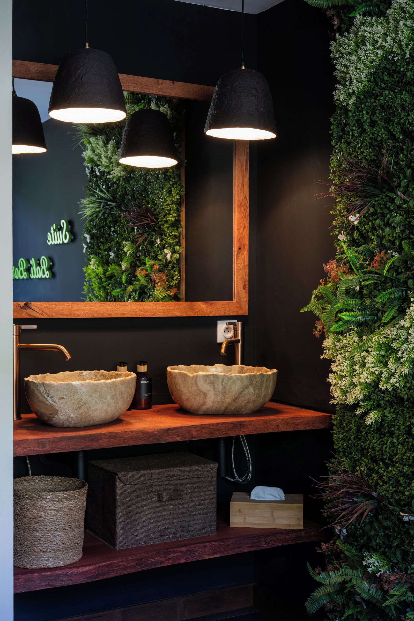 A bathroom with a wooden vanity, two stone sinks, a mirror, and black pendant lights.