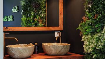 A bathroom with a wooden vanity, two stone sinks, a mirror, and black pendant lights.