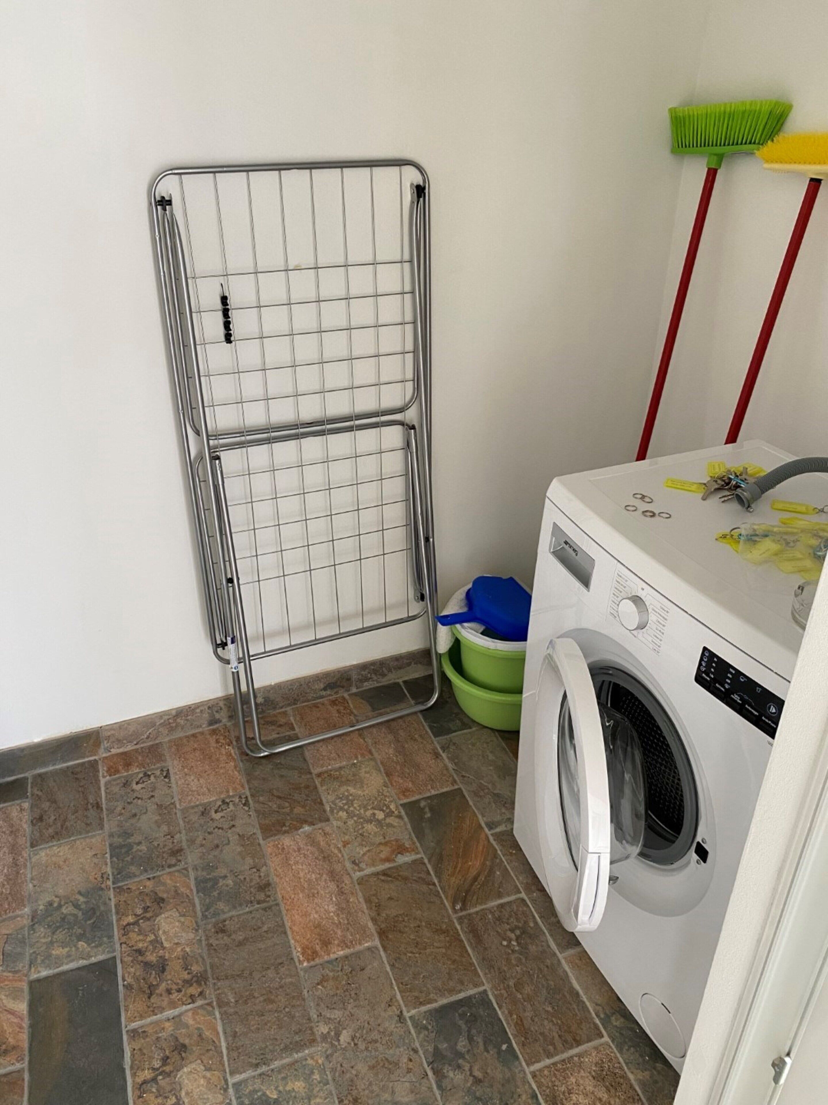 A laundry area with a metal drying rack, a washing machine, and a broom.