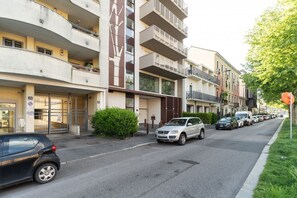 Ein mehrstöckiges Wohngebäude mit Balkonen, einem verschlossenen Eingang und parkenden Autos vor der Straße.
