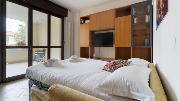 A hotel room with a bed, a TV, a sliding glass door, and a bookshelf. - Comfortable 50m2 flat for 4 people, on the 1st floor with lift.Located in the Certosa area, a neighborhood well connected to the centre, the motorways & the exhibition centres. Nearby is the historic Certosa di Garegnano, famous for its frescoes.On foot  (Milan)