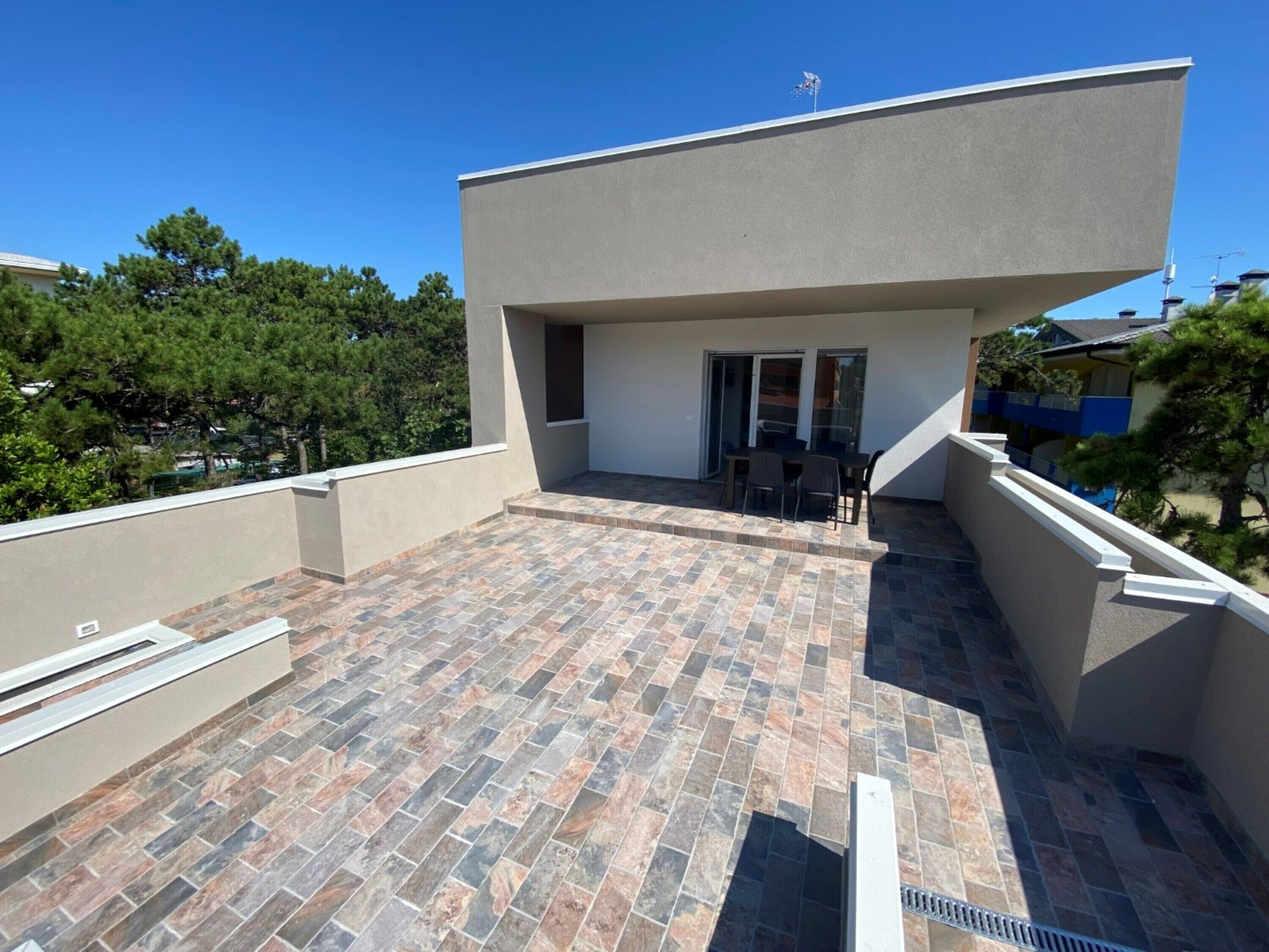 A rooftop terrace with a tiled floor, a table with chairs, and a sliding glass door leading to an indoor area.