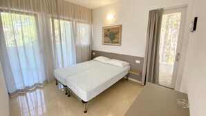 A bedroom with a bed, a bedside table, a window with curtains, and a door leading to a balcony. - Modern Studio With Spectacular Private Terrace (San Michele al Tagliamento)