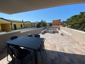 Um terraço no telhado com mesa e cadeiras, um espaço de estar integrado e vista para edifícios ao redor.