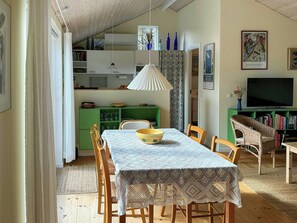 Zona pranzo con tavolo, sedie, lampada a sospensione e un armadietto verde.