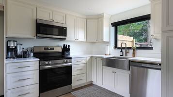 Una cocina moderna con muebles blancos, electrodomésticos de acero inoxidable y un ventanal con vistas al exterior.