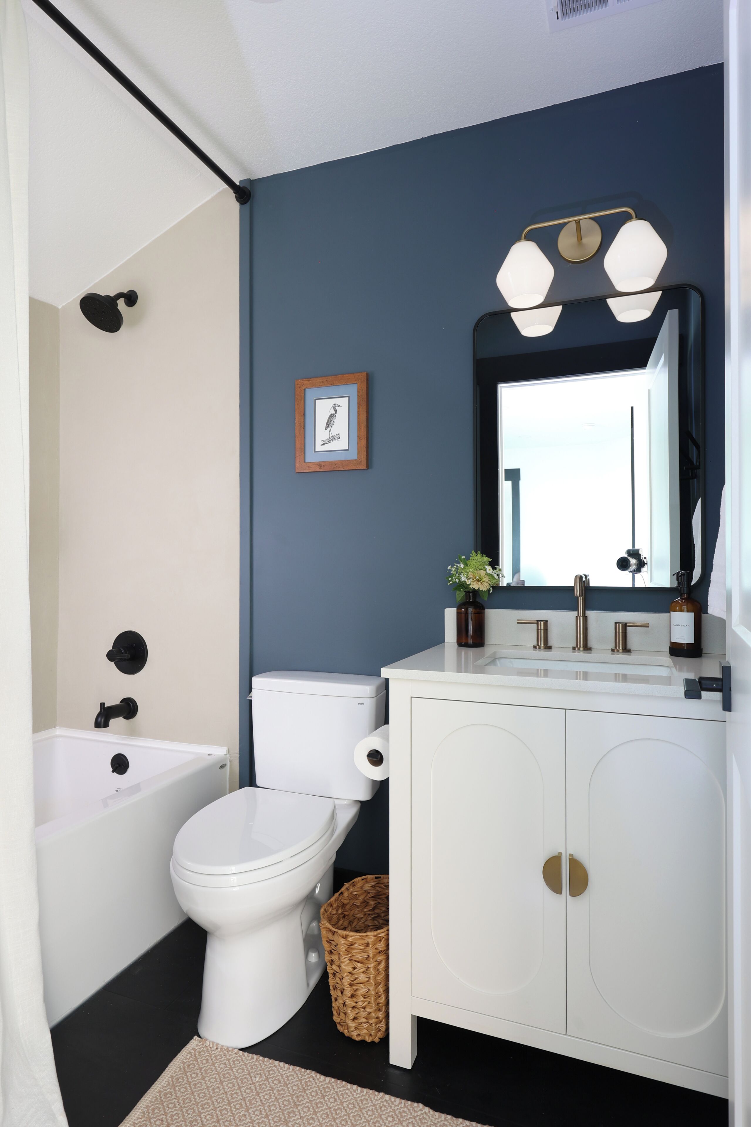 Une salle de bain moderne avec des toilettes blanches, une baignoire, un lavabo avec un miroir et un luminaire fixé au mur.