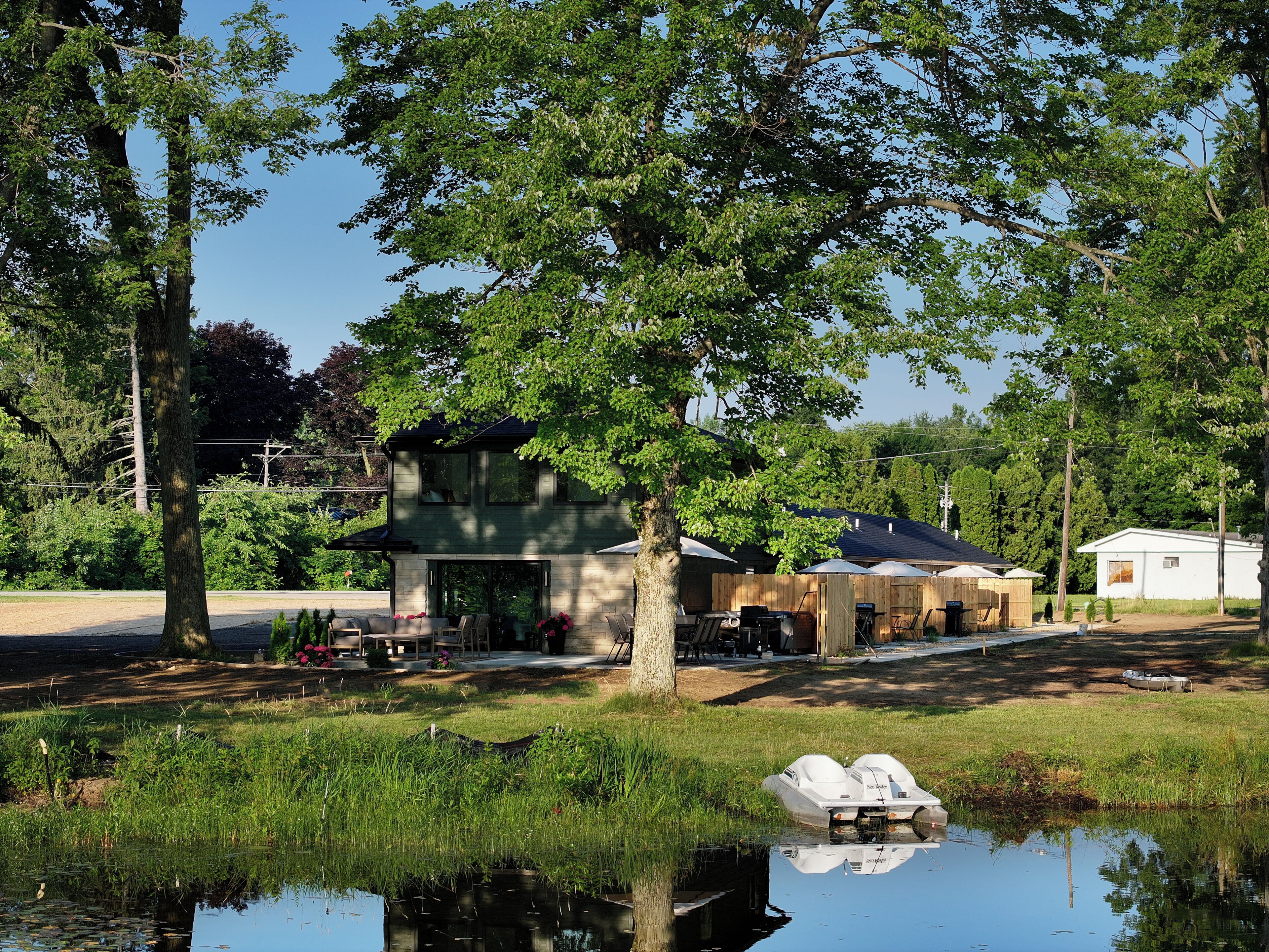 A house with a garage, a pond with a boat, and a lawn with trees.