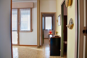 A hallway with a tiled floor, a desk with a lamp, and a door leading to another room. - A cozy and comfortable 65 square meters apartment, perfect for five people, located on the first floor of a building without an elevator.The property enjoys an excellent location in Alghero, located on the street parallel to the seafront: you can reach A (Alghero)