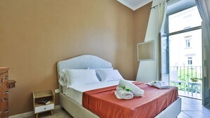 A hotel room with a bed, a wooden nightstand, a dresser, and a balcony with a railing. - Bright and welcoming apartment for three people, located in a historic building on one of Naples' most iconic streets. The two balconies overlooking the internal courtyard ensure tranquility and privacy despite its central location. It's perfect for expl (Napoli)
