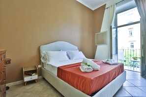 Ein Hotelzimmer mit Bett, Nachttisch aus Holz, Kommode und Balkon mit Geländer.