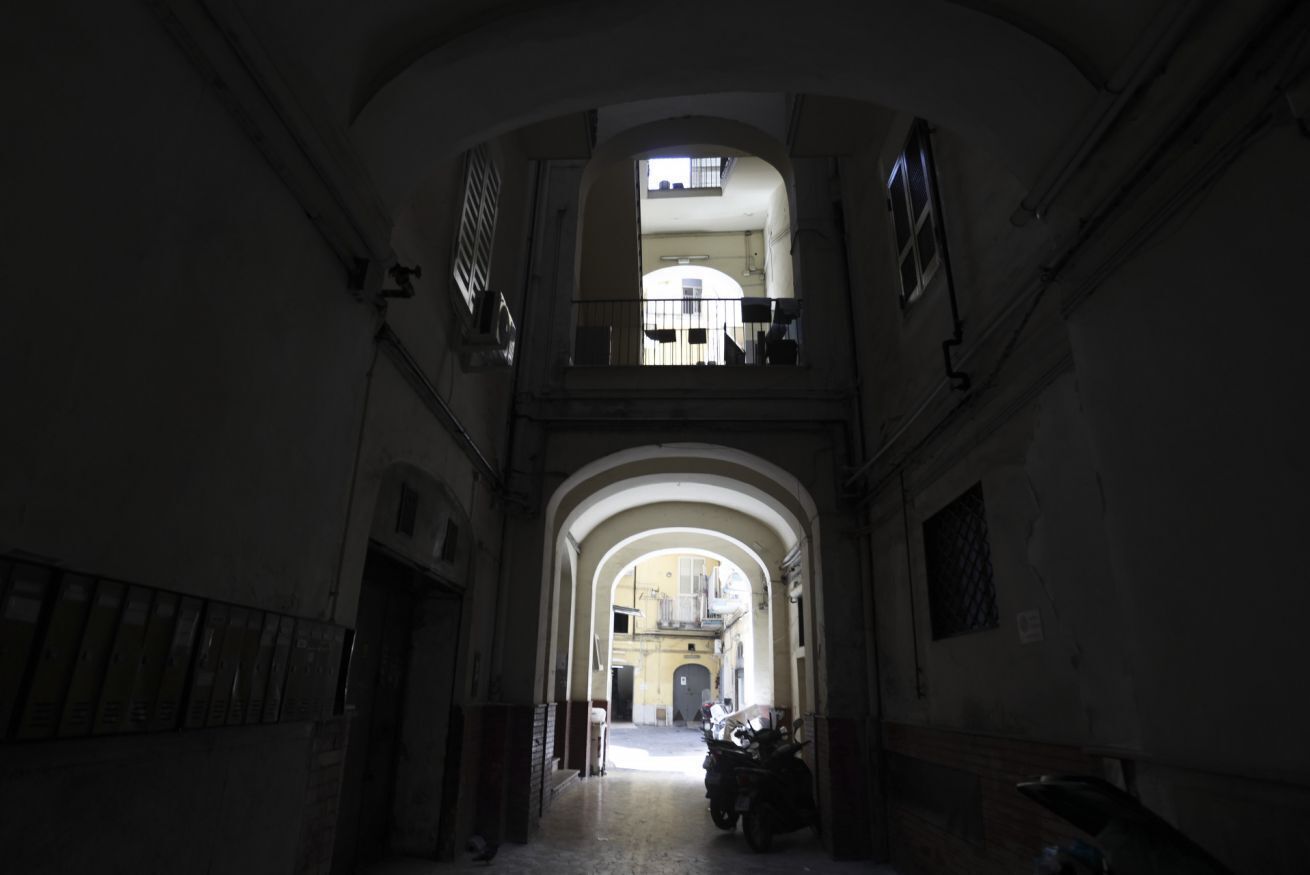 A corridor with an arched ceiling, a motorcycle parked at the end, and a balcony with a railing.