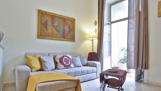 A living room with a sofa, a table, a lamp, and a large window. - Bright and welcoming apartment for three people, located in a historic building on one of Naples' most iconic streets. The two balconies overlooking the internal courtyard ensure tranquility and privacy despite its central location. It's perfect for expl (Napoli)