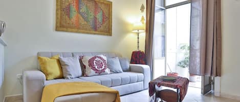 A living room with a sofa, a table, a lamp, and a large window.