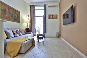 Ein Wohnzimmer mit einer Couch, einem Couchtisch, einem an der Wand montierten Fernseher und einem Fenster mit Vorhängen.