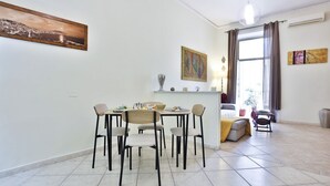 A dining area with a table and chairs, a window with curtains, and a painting on the wall. - Bright and welcoming apartment for three people, located in a historic building on one of Naples' most iconic streets. The two balconies overlooking the internal courtyard ensure tranquility and privacy despite its central location. It's perfect for expl (Napoli)