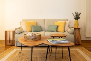 Ein Wohnzimmer mit einer Couch, zwei runden Holztischen, einem gewebten Korb und einem kleinen Holznachttisch mit einer Pflanze.