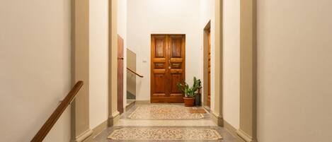 A hallway with a wooden door at the end, a potted plant, and a carpeted staircase.