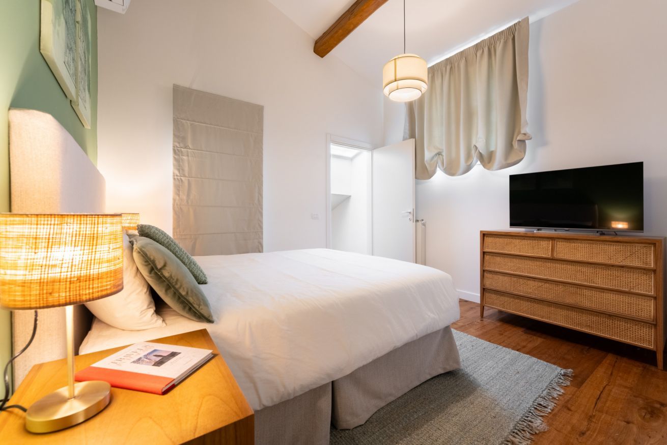 A bedroom with a bed, bedside lamp, dresser, and TV.