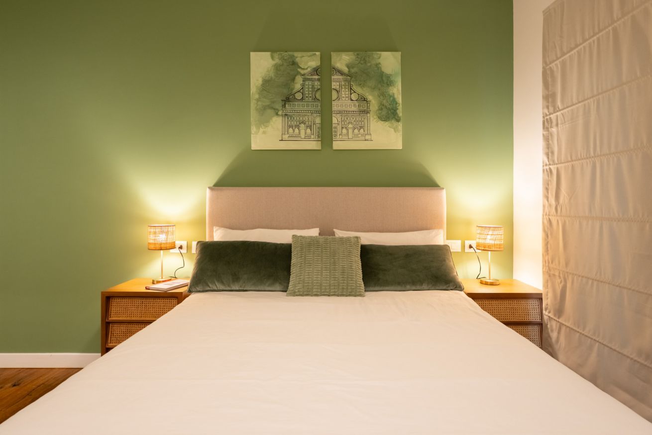 A bed with a white mattress, two pillows, a green throw, and two bedside lamps.
