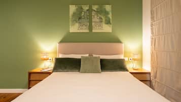 A bed with a white mattress, two pillows, a green throw, and two bedside lamps.