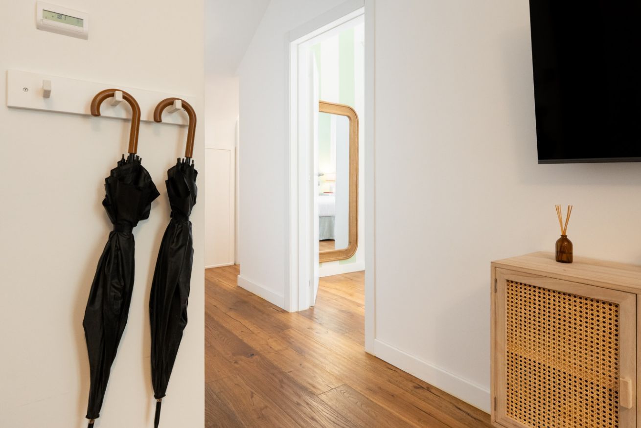 A hallway with wooden flooring, a wall-mounted TV, and a door leading to another room.