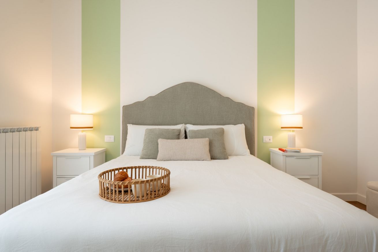 Un letto rifatto con un poggiatesta, due comodini con lampade e un cesto in vimini sul letto.