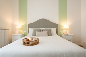 Un lit bien fait, avec une tête de lit, deux tables de chevet avec des lampes et un panier en osier posé sur le lit.