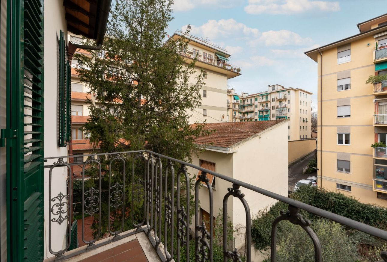 A residential building with balconies, a staircase, and a tree in the foreground.
