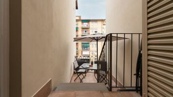 Un corridoio stretto con una scala che porta a un balcone con mobili da esterno e un tavolo.
