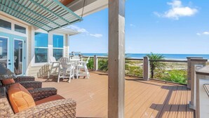 Um deck de madeira com móveis ao ar livre, uma área coberta e vista para a praia.