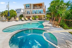 Ein Pool mit geschwungener Form, umgeben von Liegestühlen und einem mehrstöckigen Gebäude im Hintergrund.