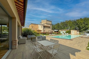 Un área junto a la piscina con mobiliario exterior, una piscina y un edificio al fondo.