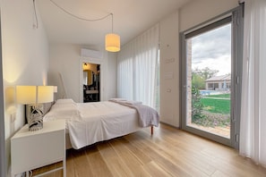 Un dormitorio con cama, mesita de noche, lámpara y vistas al exterior por un ventanal corredera.