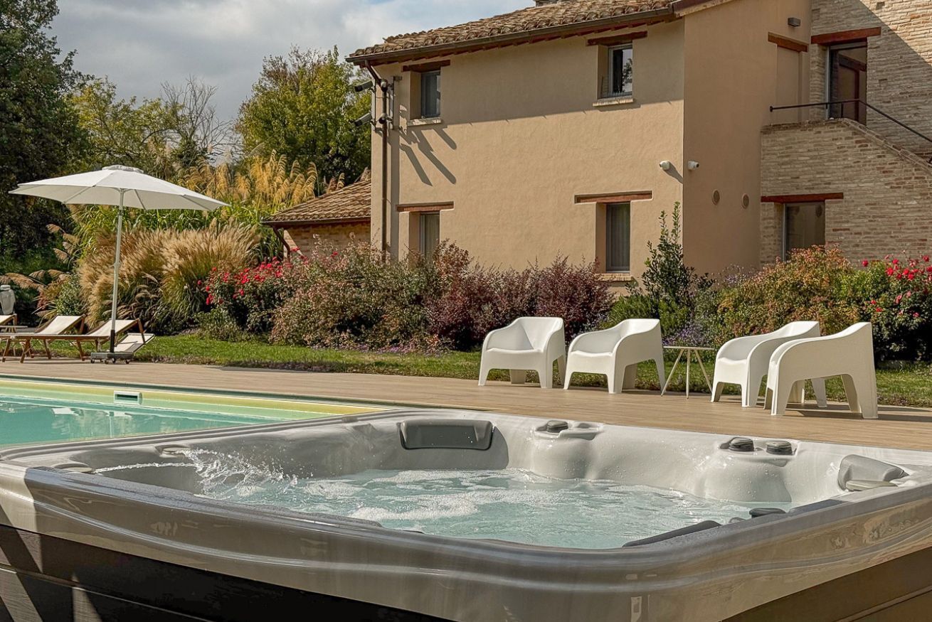 Ein Whirlpool, Sitzmöglichkeiten im Freien und ein Poolbereich mit einem Gebäude im Hintergrund.