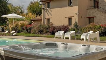 Ein Whirlpool, Sitzmöglichkeiten im Freien und ein Poolbereich mit einem Gebäude im Hintergrund.