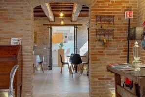 Un interno con pareti in mattoni a vista, un tavolo di legno con sedie e un lampadario.
