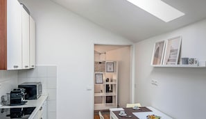 A compact kitchen with white cabinets, a microwave, and a dining area with a table and chairs. - [Above the rooftops] Real Ligurian Caruggio (Varazze)