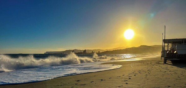 A beach with waves, a lifeguard tower, and a sunset.