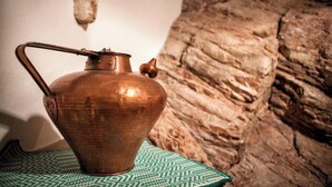 Una olla de coure sobre un mantell estampat, una paret de pedra i una fotografia emmarcada a la paret.