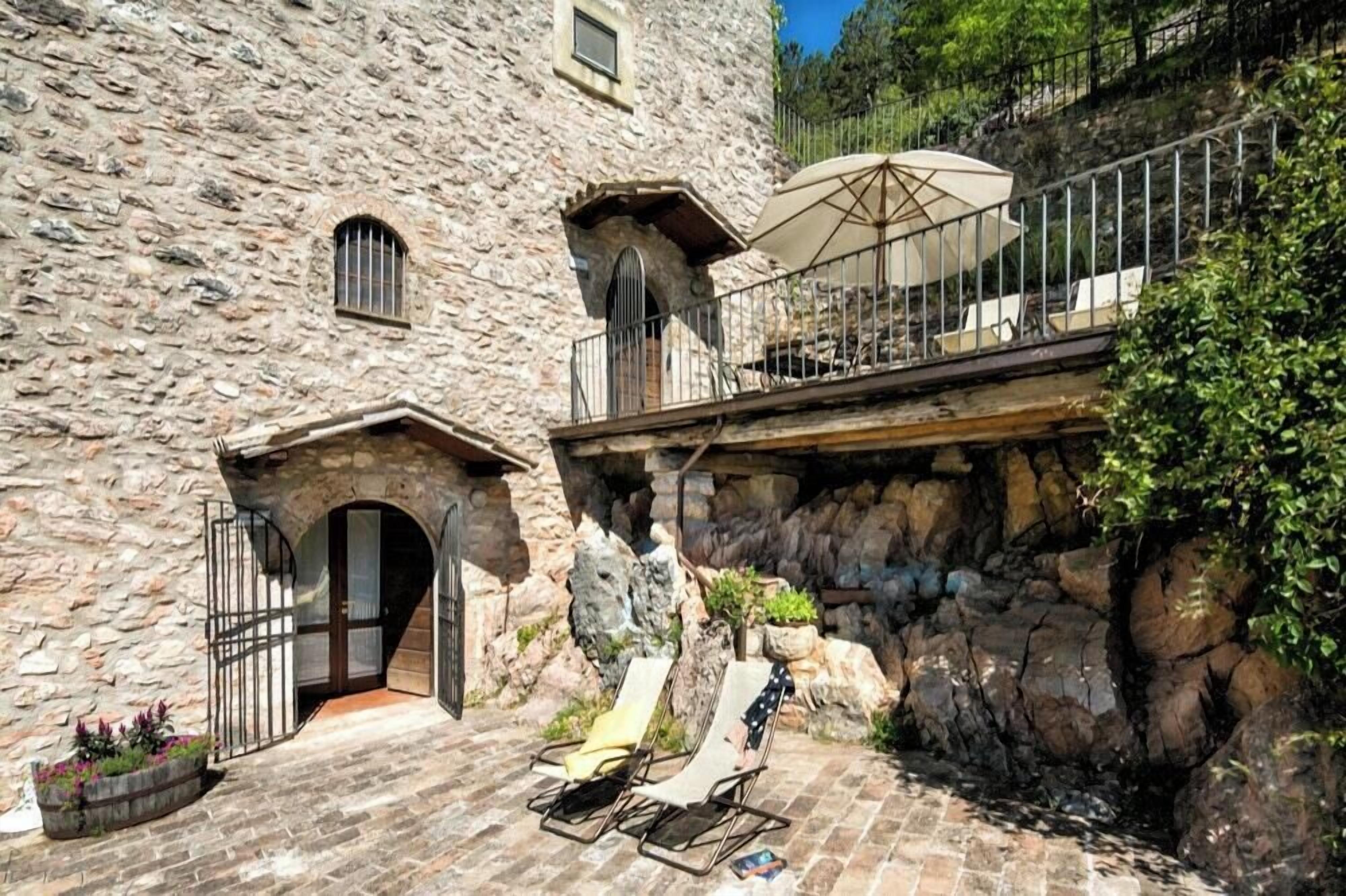 Een stenen gebouw met een balkon, terras en een kleine waterval.