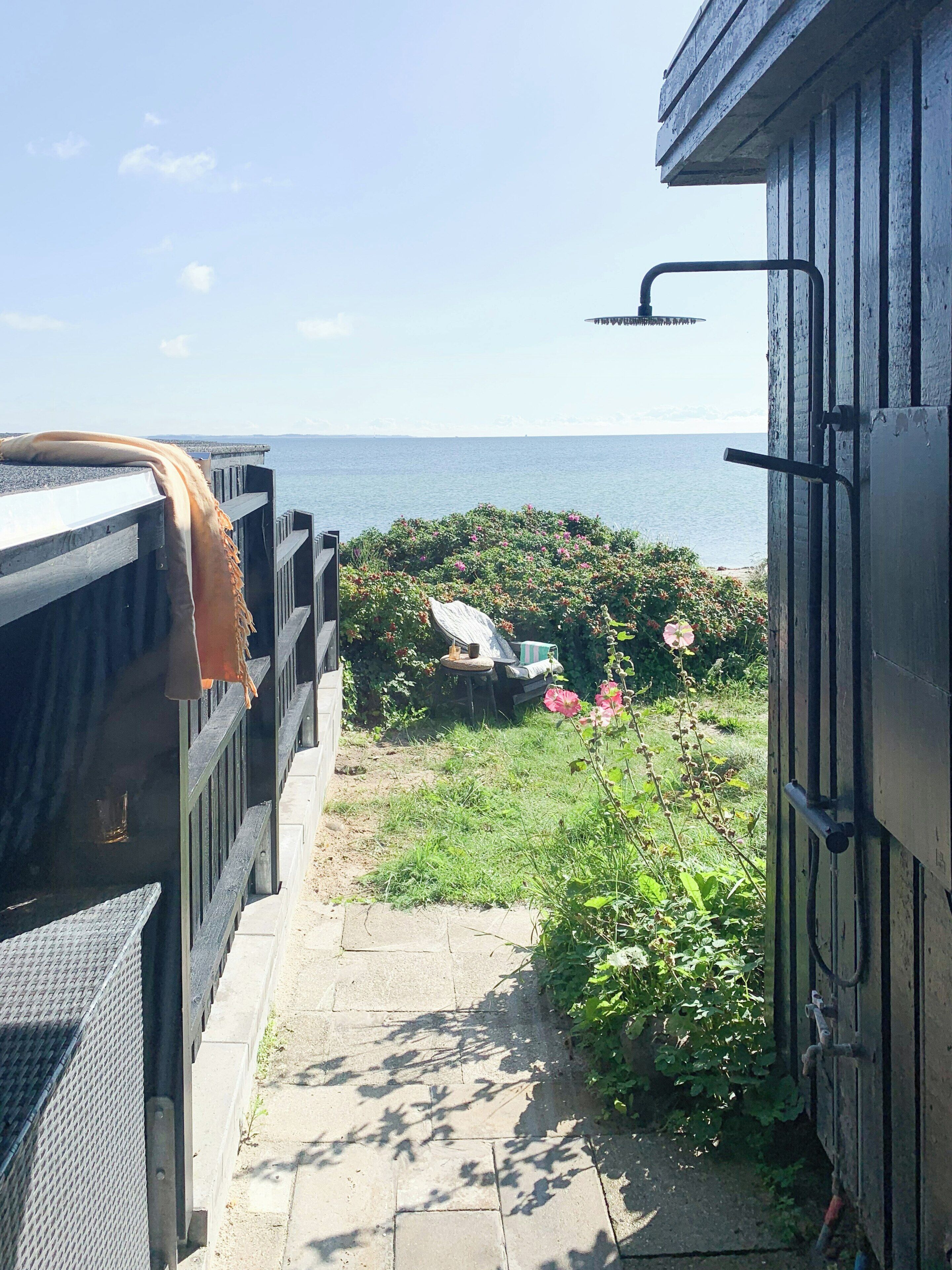 A pathway leading to a garden with a view of the sea, a wooden structure with a metal door, and a metal railing.