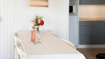 A dining table with a white tablecloth, a wicker hanging light, and a vase with flowers.